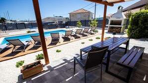 Un patio con piscina, sillas de descanso, mesa y una parrilla.