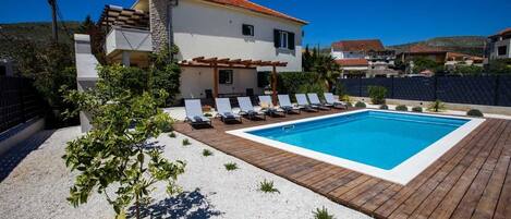 Una piscina con sillones reclinables, una pérgola y un edificio blanco con techo rojo.
