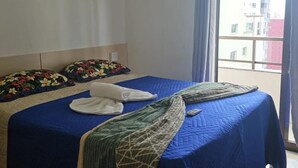 Ein Hotelzimmer mit einem Bett, das mit einer blauen Bettdecke, zwei floralen Kissen und einer grünen Tagesdecke bezogen ist.