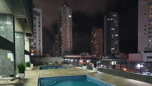Ein Poolbereich auf dem Dach mit mehreren Pools und Liegestühlen, umgeben von Hochhäusern bei Nacht.