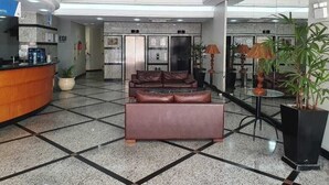 Eine Lobby mit einer Rezeption, einer Sitzecke mit Ledersofas, einer großen Topfpflanze und einer Glaswand.