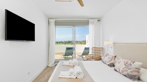 Et hotelværelse med seng, fjernsyn, loftventilator, balkon med stole og udsigt til det fri.