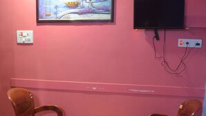 A room with a pink wall, a wooden table, two wooden chairs, a painting, and a television. - Hotel Dream Star  (Sahibganj)