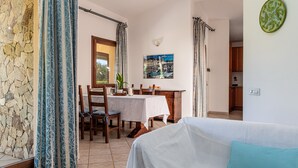 A room with a dining table, chairs, a bed, a window, and a wall-mounted light fixture. - Villa 'Mariella' with Private Terrace, Wi-Fi and Air Conditioning (Costa Rei)