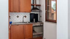 A compact kitchen with wooden cabinets, a stainless steel stove, a sink, and a window. - Villa 'Mariella' with Private Terrace, Wi-Fi and Air Conditioning (Costa Rei)