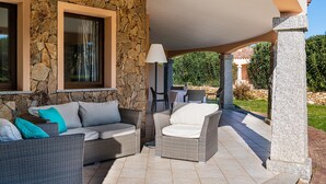 A covered outdoor seating area with wicker furniture, stone walls, and a lamp. - Villa 'Mariella' with Private Terrace, Wi-Fi and Air Conditioning (Costa Rei)