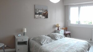 A bedroom with a bed, a nightstand, a lamp, a chair, a window, and a painting on the wall. - T2 apartment 200 m from the sea (Concarneau)