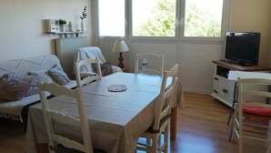 A dining area with a table, chairs, a lamp, and a television. - T2 apartment 200 m from the sea (Concarneau)