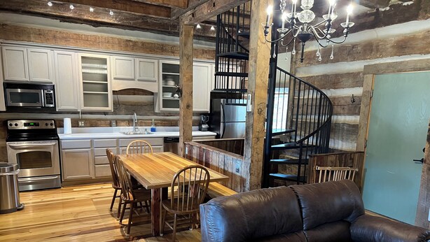 A rustic kitchen with wooden cabinets, a dining table, and a leather sofa. - Historic Cabin in the Blue Ridge Mountains (Pearisburg)