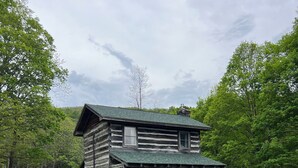 A rustic log cabin with a porch, surrounded by a grassy field and trees. - Historic Cabin in the Blue Ridge Mountains (Pearisburg)