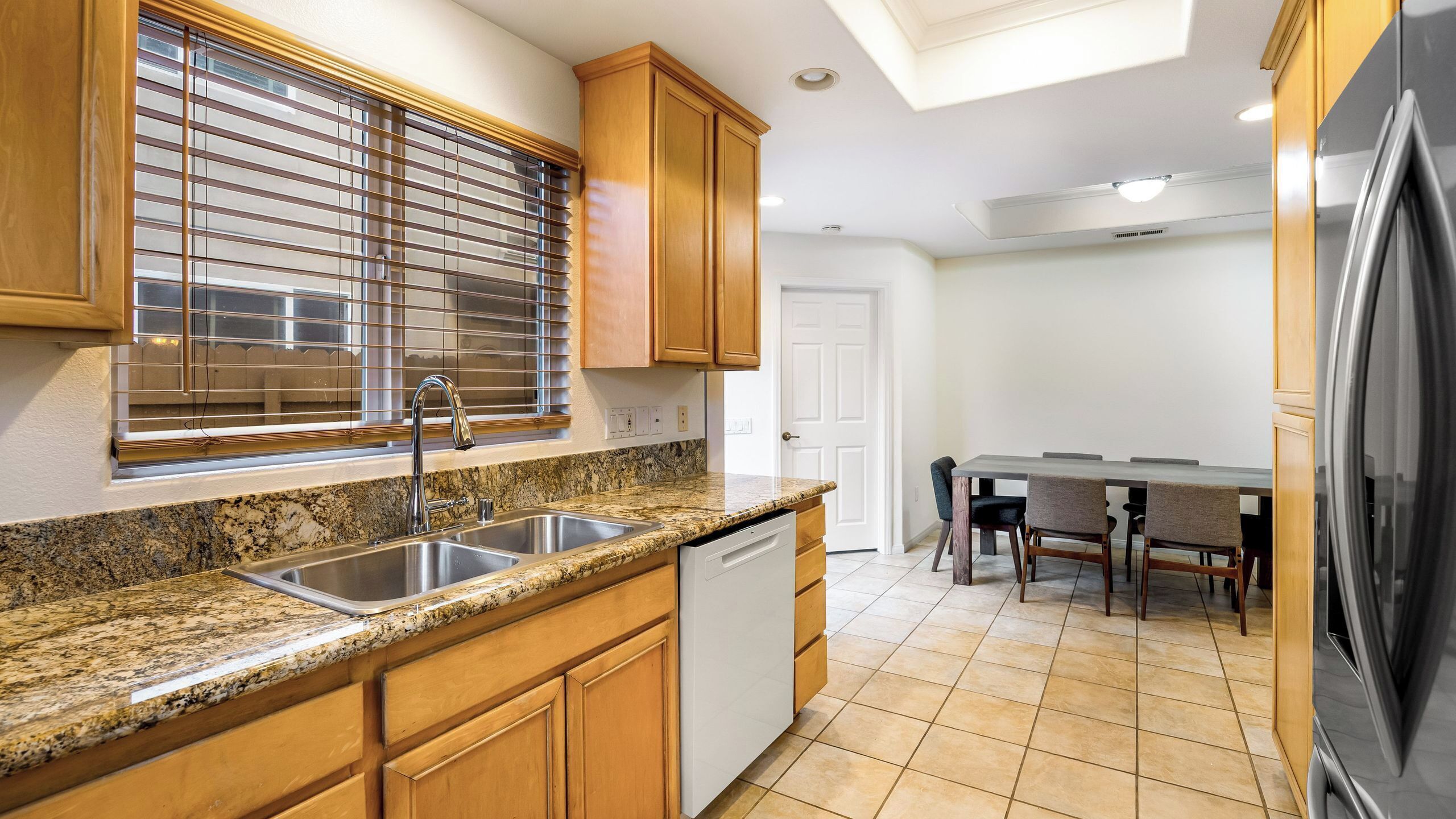 A kitchen with granite countertops, wooden cabinets, a stainless steel sink, and a dishwasher.