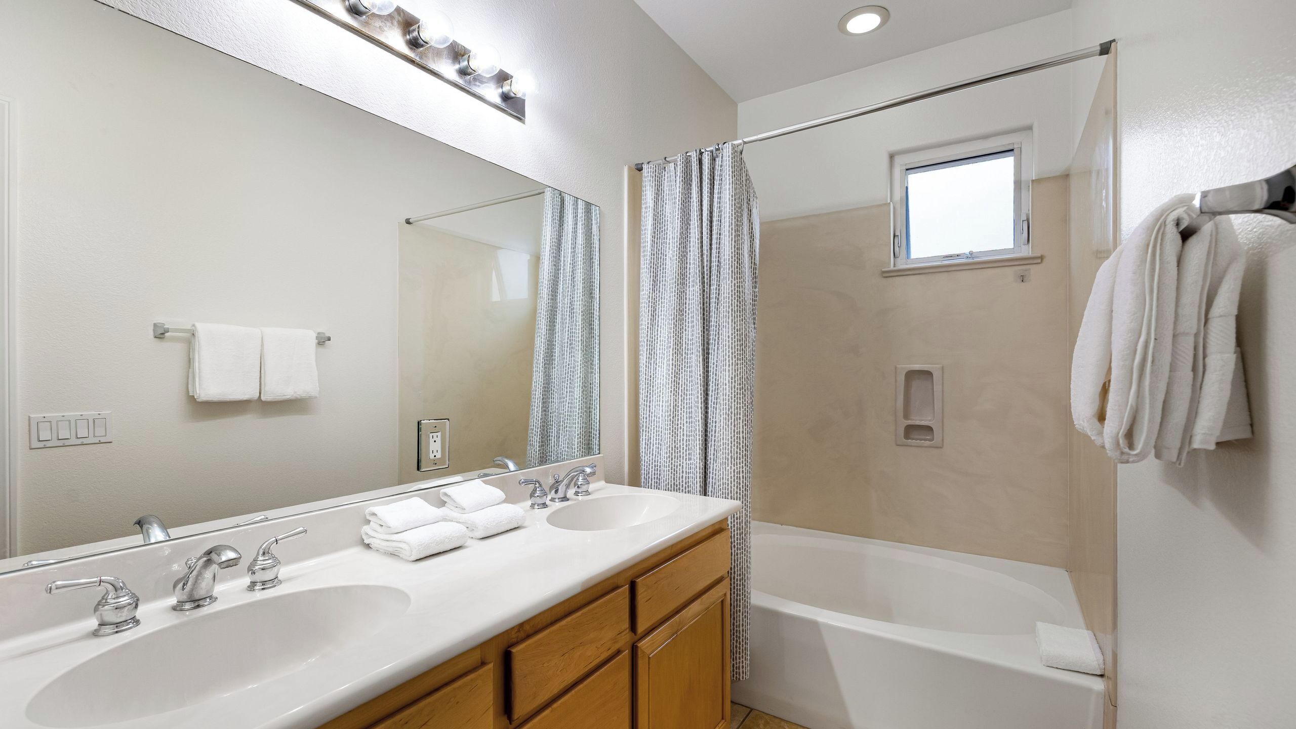 A bathroom with two sinks, a mirror, a shower, and a window.