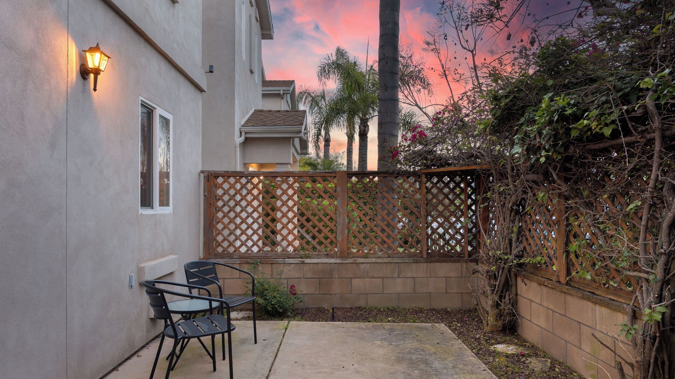 A patio with a wooden fence, a chair, and a wall-mounted light fixture.