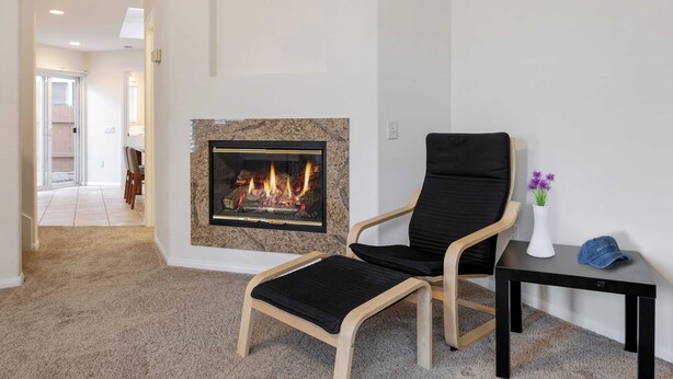 A living room with a fireplace, a black chair, a small table with a vase and a cap, and a carpeted floor. - Walk to Dining, Mission + Pacific Beach, and Bars/nightlife Private Backyard (San Diego)