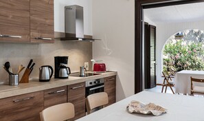 Una cocina moderna con estufa a gas, cafetera y tostadora. Hay una zona de comedor con mesa y sillas.