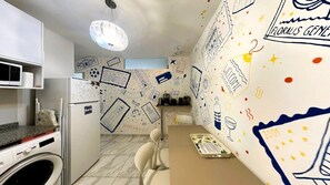 A compact kitchen with a microwave, refrigerator, and washing machine. There is a dining table with chairs and a decorative wall with doodles and text. - Experience Buenos Aires · Central & Artistic (Buenos Aires)