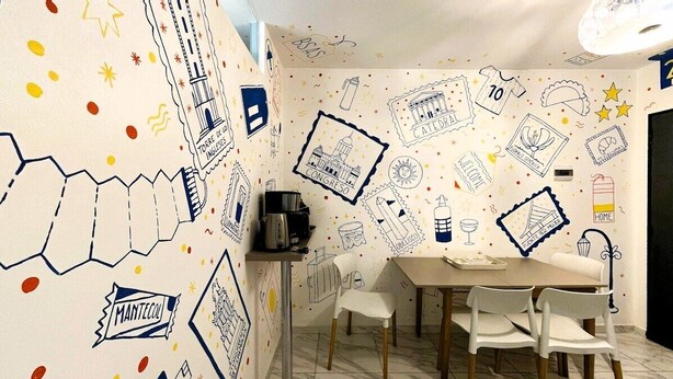 A dining area with a table, chairs, and a coffee machine. The walls are decorated with various doodles and text.