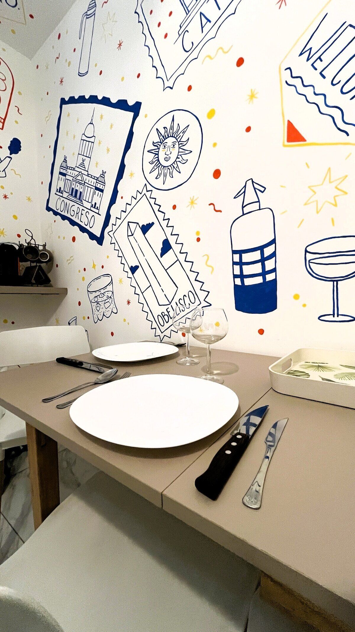 Comedor con una mesa dispuesta para dos personas, con un plato blanco, una copa de vino y cubiertos.
