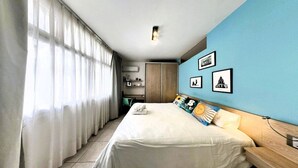 A hotel room with a bed, curtains, a wardrobe, a desk, and wall art.