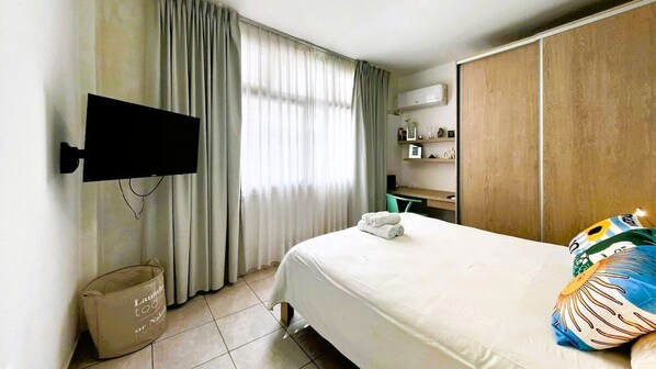 A hotel room with a bed, a television mounted on the wall, a desk, and a wardrobe.