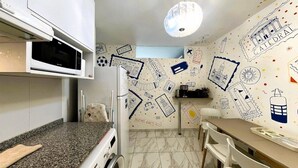 A kitchen with a microwave, a coffee machine, and a sink. There is a dining table with chairs. The walls are decorated with doodles and text.