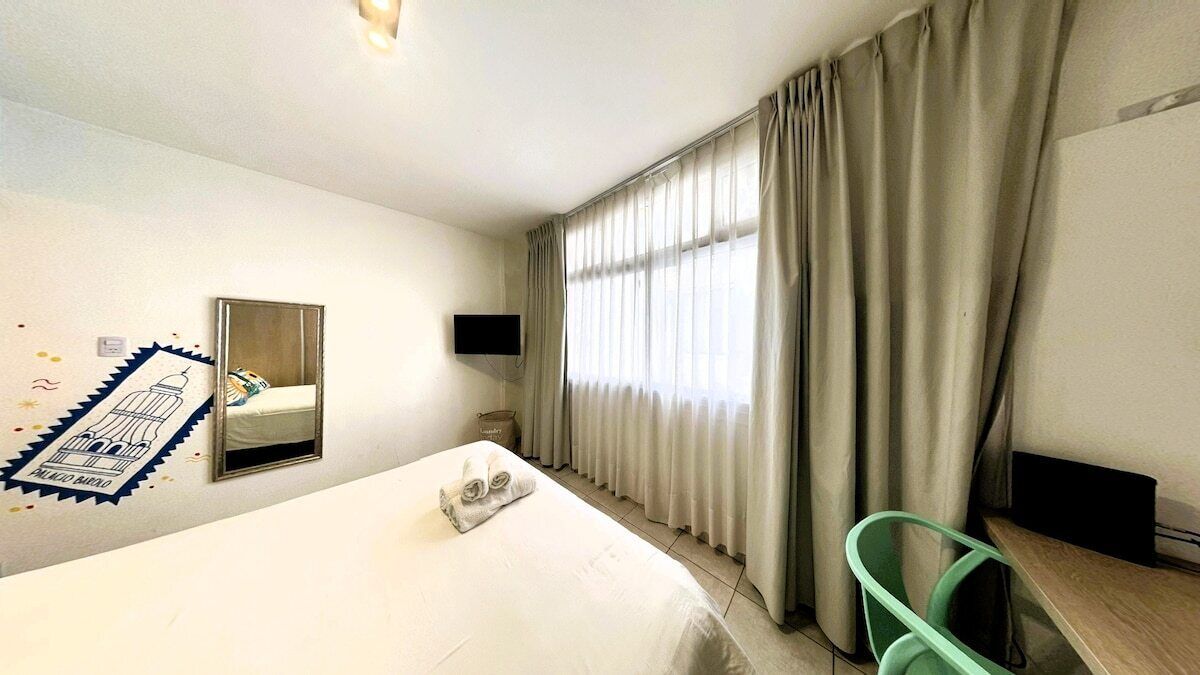 Una habitación de hotel con una cama, un escritorio, una silla, un televisor y cortinas.