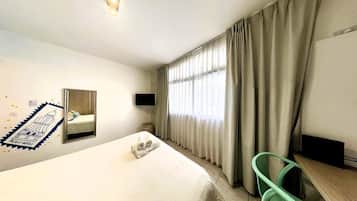 Una habitación de hotel con una cama, un escritorio, una silla, un televisor y cortinas.