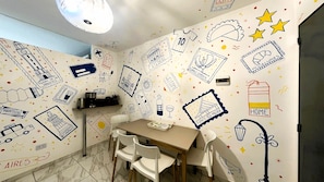 Uma área de refeições com uma mesa, cadeiras e um painel decorado com vários desenhos e ilustrações.