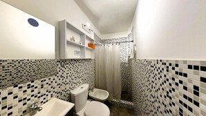 A bathroom with a toilet, bidet, sink, and a shower area with a curtain.
