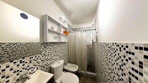 Een badkamer met toilet, bidet, wastafel en een douchecabine met gordijn.