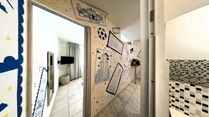 Un couloir dont un mur est décoré de divers autocollants et dessins, avec un téléviseur fixé au mur et un sol carrelé.