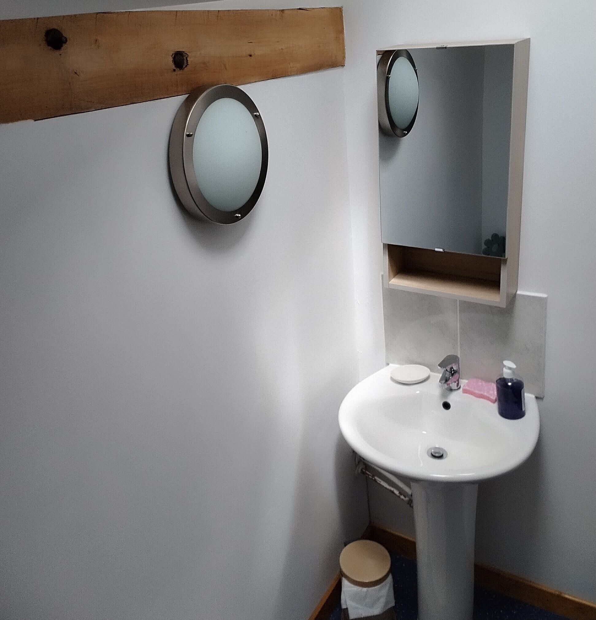 A bathroom with a white sink, a mirror, and a wooden shelf above the sink.