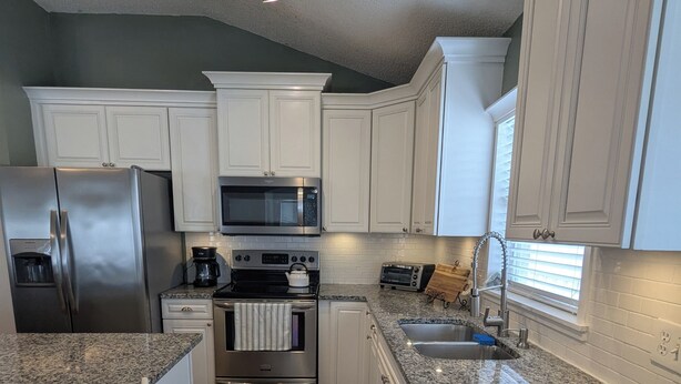 A modern kitchen with white cabinetry, stainless steel appliances, a granite countertop, and a wooden floor. - The Garden House - 3BR /6 Guests (Lutz)