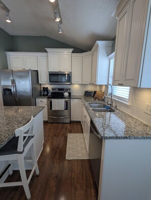 A modern kitchen with white cabinetry, stainless steel appliances, a granite countertop, and a wooden floor. - The Garden House - 3BR /6 Guests (Lutz)