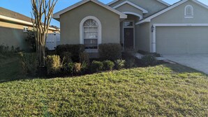 A residential house with a garage, a front yard with grass and shrubs, and a clear blue sky. - The Garden House - 3BR /6 Guests (Lutz)