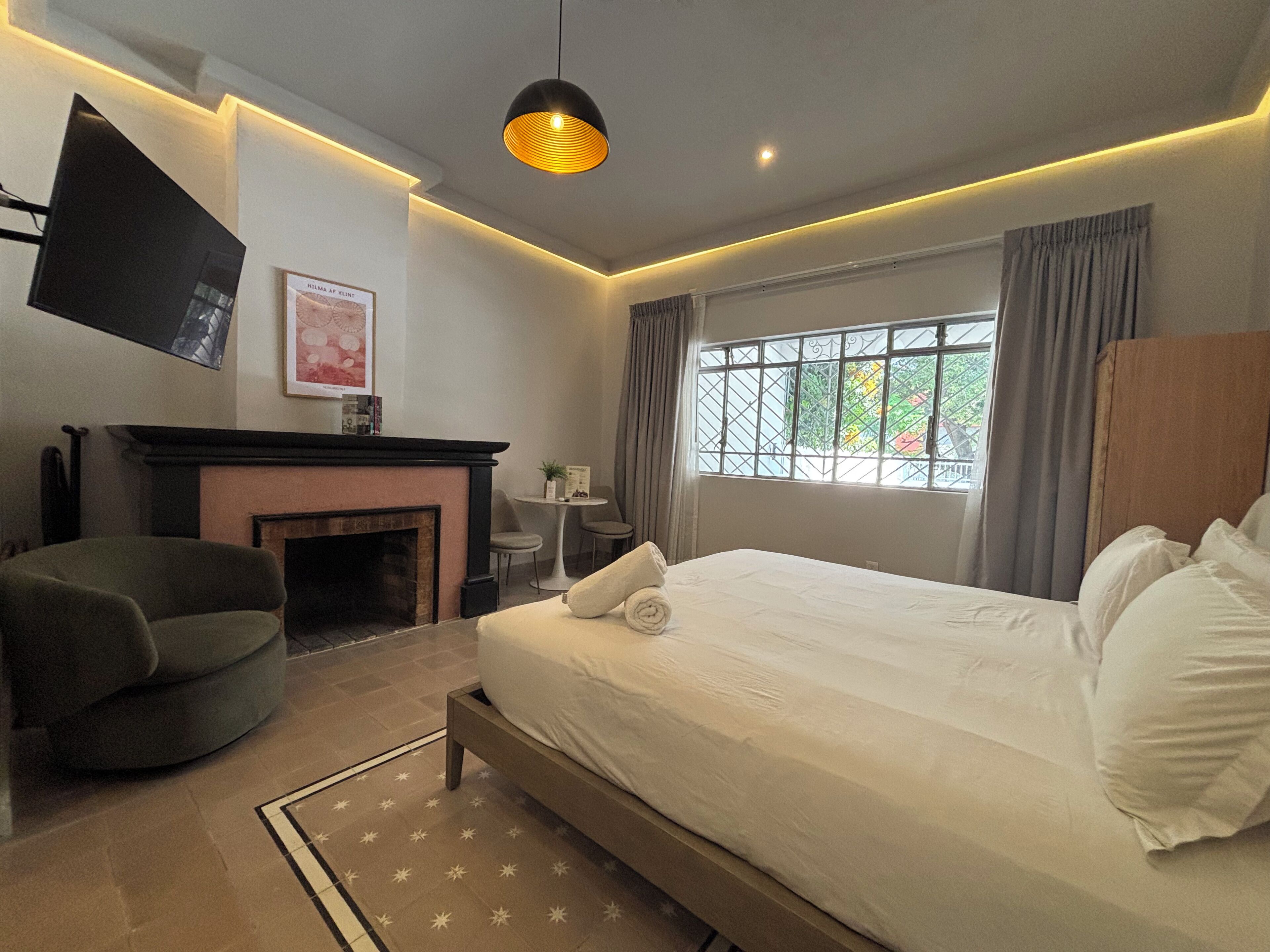 A modern bedroom with a large bed, a fireplace, a flat-screen TV, and a window with curtains.
