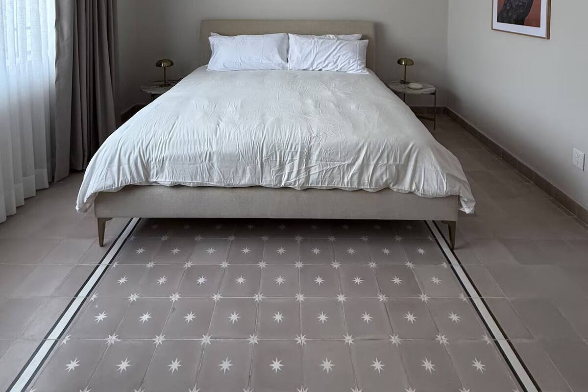 A bedroom with a bed, bedside tables, a hanging lamp, a framed picture on the wall, and a star-patterned rug.