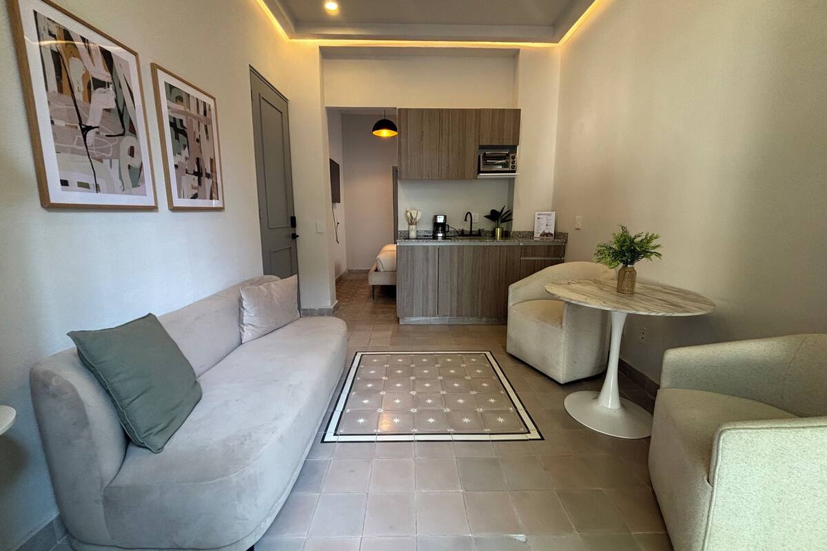 A modern living room with a sofa, a coffee table, and a dining area with a kitchen in the background.