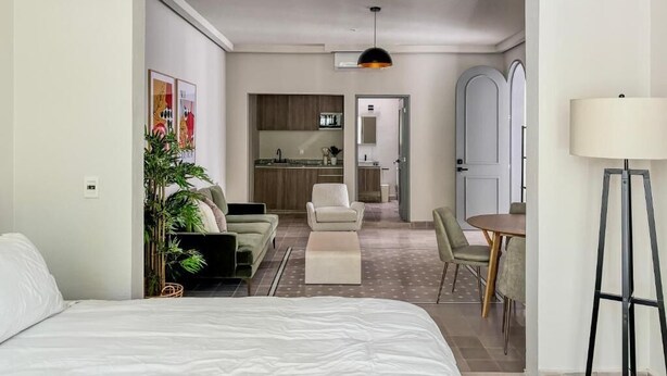 A modern hotel room with a large bed, a dining area with a table and chairs, a kitchen in the background, and a hallway leading to another room. - Casa Mia  (Guadalajara)
