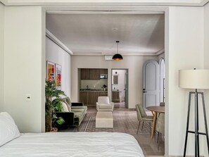 Una moderna camera d'albergo con un grande letto, un'area pranzo con tavolo e sedie, una cucina sullo sfondo e un corridoio che conduce a un'altra stanza.