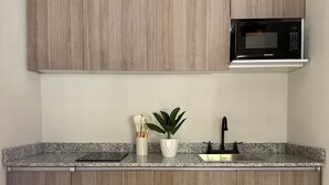 A kitchen with wooden cabinets, a granite countertop, a microwave, a sink, and a potted plant. - Casa Mia  (Guadalajara)