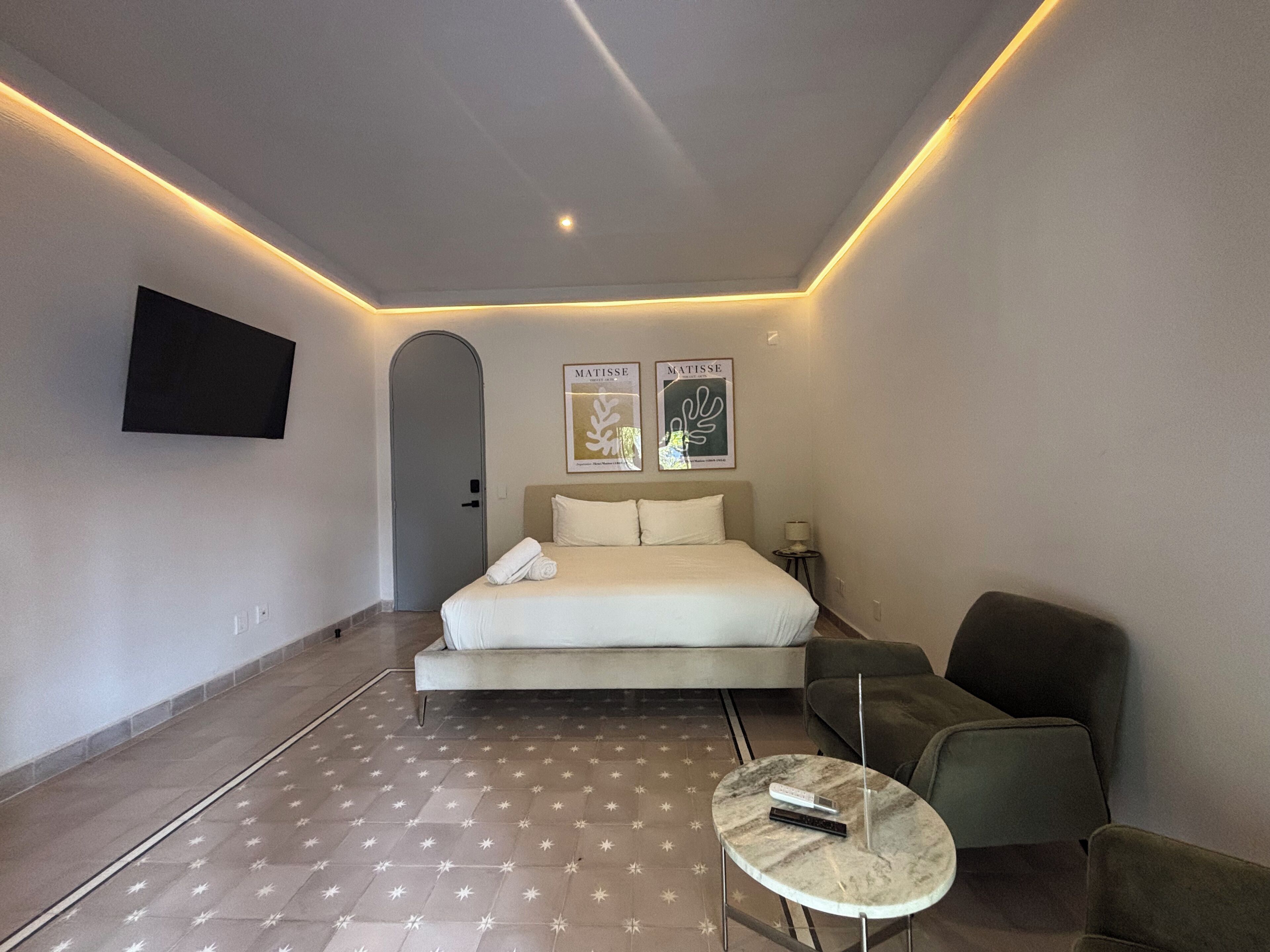 Une chambre d’hôtel moderne dotée d’un grand lit, d’un téléviseur à écran plat fixé au mur et d’une petite table ronde avec une télécommande.