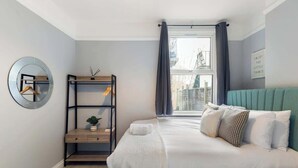 A bedroom with a bed, a bedside table, a mirror, and a window with curtains.