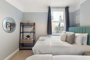 A bedroom with a bed, a bedside table, a mirror, and a window with curtains.