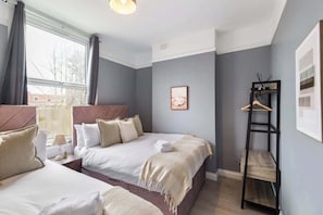 Hotellihuone, jossa on kaksi sänkyä, ikkuna, seinälle kiinnitetty hylly ja kehystetty taulu.