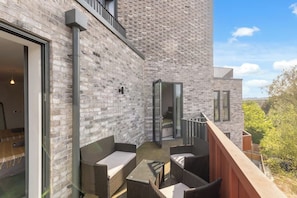 A modern building with a brick exterior, a balcony with wicker furniture, and a glass door leading to an interior space. - Apartment near Wembley with Patio & Free Parking (Greater London)