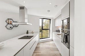 A modern kitchen with white cabinetry, a black countertop, a window with a view, and a built-in oven. - Apartment near Wembley with Patio & Free Parking (Greater London)