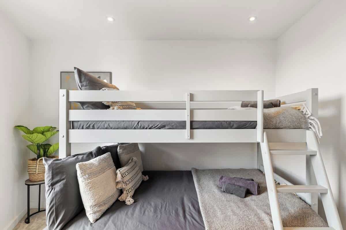A bunk bed room with a small table, a potted plant, and a ladder.