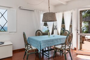 Zona pranzo con tavolo ricoperto da tovaglia fantasia, sedie in vimini e lampadario.