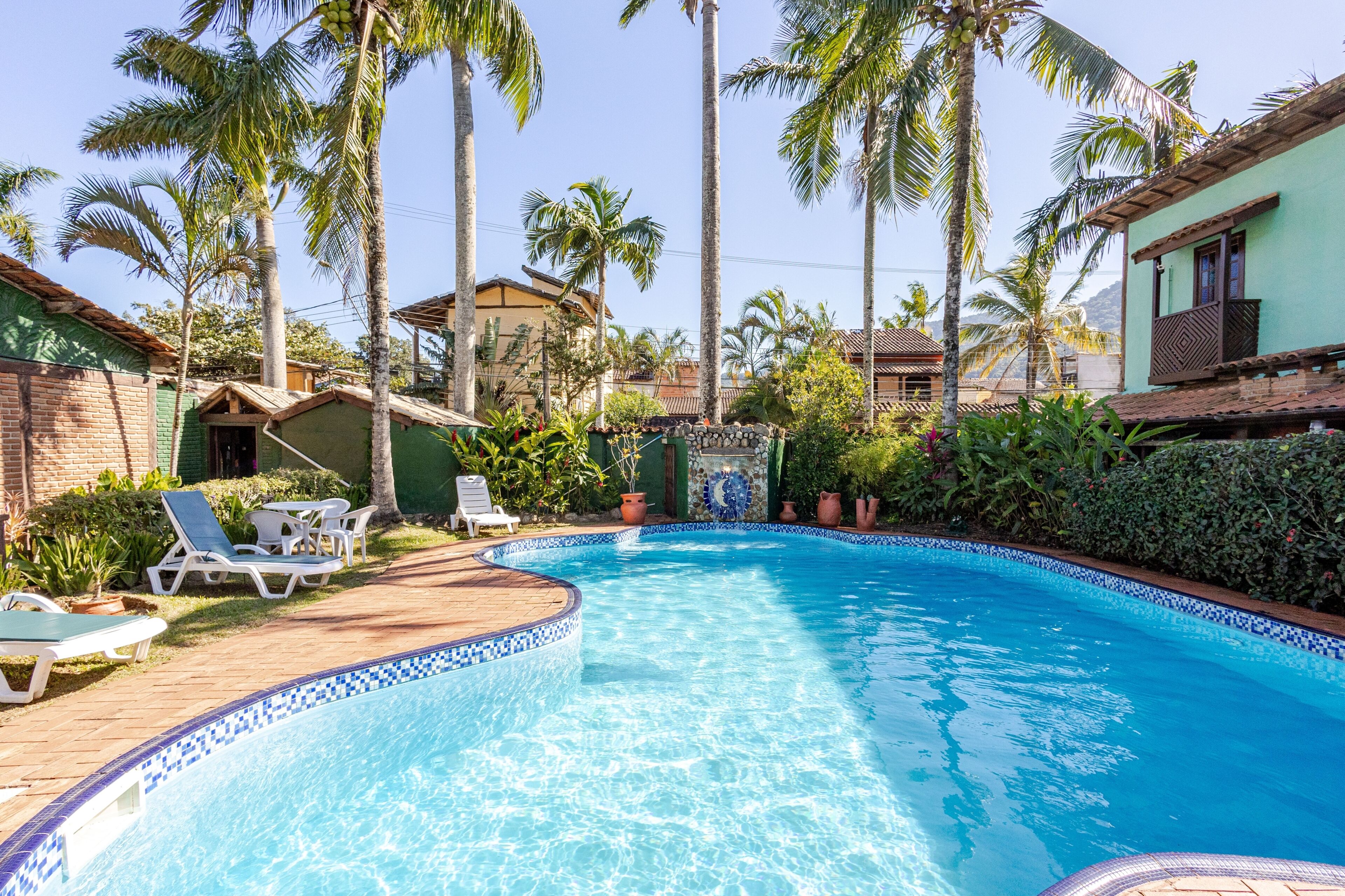 A swimming pool with a tiled edge, surrounded by palm trees and a brick wall.